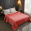 A plush velvet quilted bed cover blanket in coral pink is displayed on a bed in a modern bedroom.