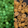 A close-up view of a pack of 3mm glow-in-the-dark green glass seed beads.