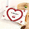 A white cushion cover featuring a red heart outline and cherry designs on a light beige woven surface.