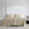 A beige luxury organic bamboo bed sheet set draped over a bed in a bright, minimalist room.