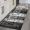 A long, rectangular kitchen mat with a distressed black and white design is placed on a wooden floor.