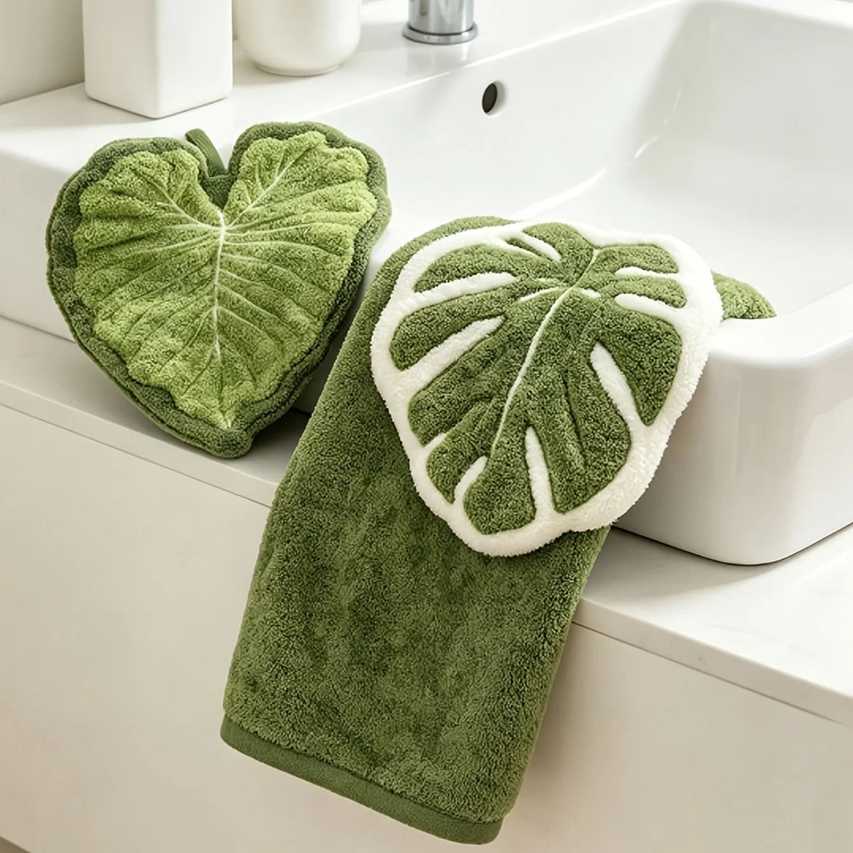 A green leaf-shaped hand towel with white trim is displayed on a white bathroom sink.