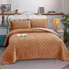 A plush velvet quilted bed cover blanket in a warm tan color spread across a bed.