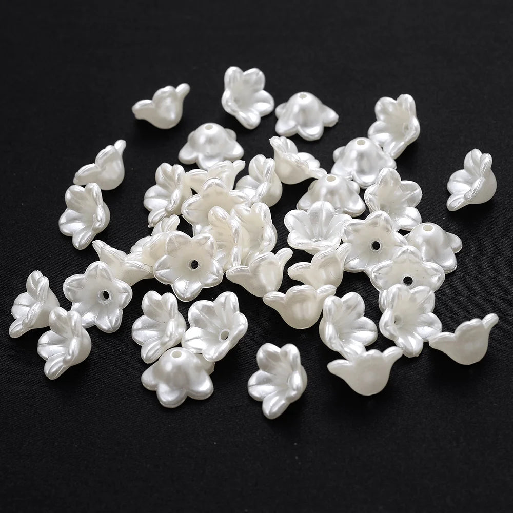 A collection of small, white imitation pearl flower spacer beads scattered on a dark surface.