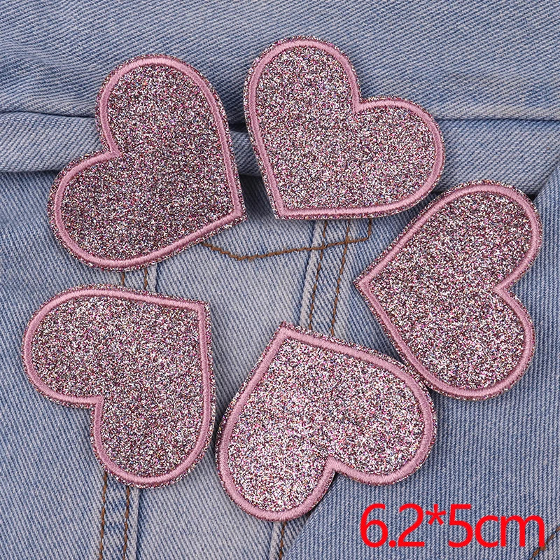 Five pink glitter heart-shaped iron-on patches arranged in a circle on a denim fabric background.