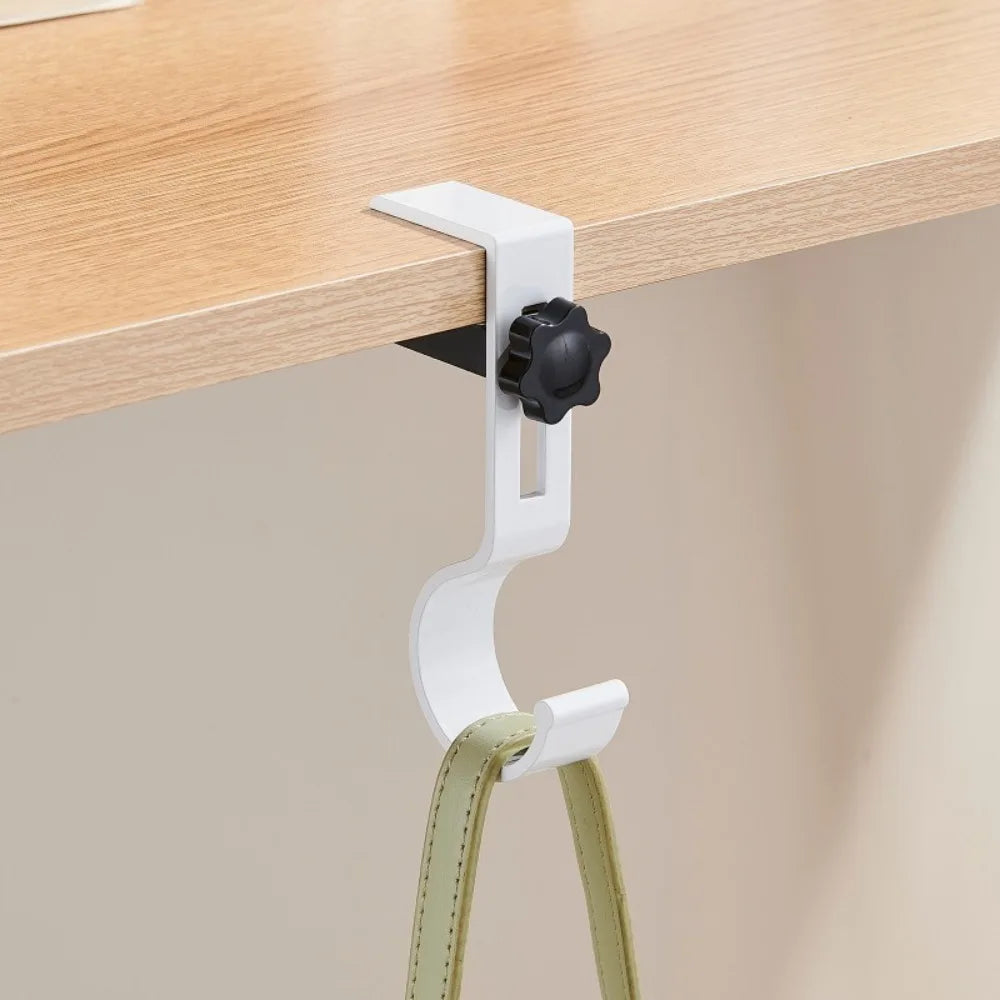 A white adjustable desk hook with a black clip is mounted on a wooden desk surface.