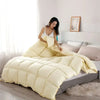 A fluffy cream colored goose down comforter duvet is displayed on a bed in a bright room.