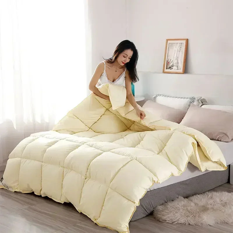 A fluffy cream colored goose down comforter duvet is displayed on a bed in a bright room.