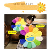 A plush sunflower cushion with a smiling face is displayed against a dark background.