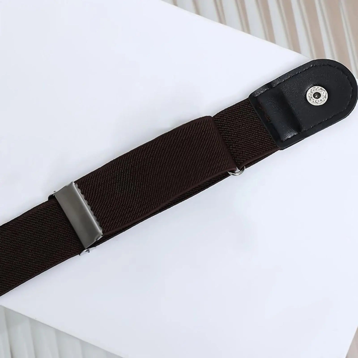 A black stretchable elastic belt with a silver buckle is shown on a white surface.