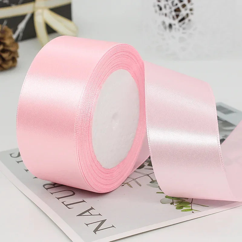 Roll of pink satin craft ribbon with a white core shown on a white surface.