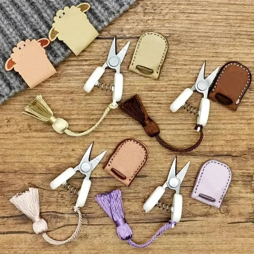 A collection of mini precision sewing scissors in various colors and styles with protective leather covers on a wooden surfac