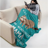 A person is relaxing on a sofa with a teal knit throw blanket featuring a sloth and text.