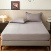 A neatly made bed with a light gray fitted sheet and pillow on a wooden frame.