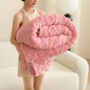 A woman is holding a pink coral fleece blanket with a quilted texture.