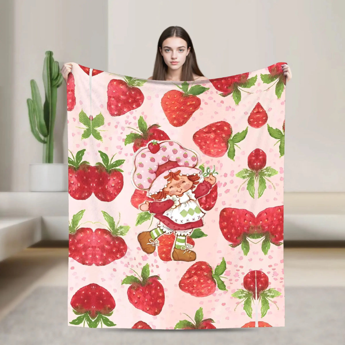 A pink strawberry print throw blanket featuring a cartoon strawberry shortcake character.