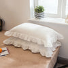 A set of two white washed cotton pillowcases with ruffled edges displayed on a wooden surface.