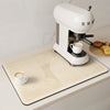 A white espresso machine is placed on a beige kitchen drain mat with coffee cups and toast visible.