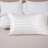 White satin pillow covers with thin vertical stripes arranged on a light beige surface.