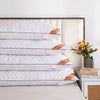 A stack of white quilted rectangle sleeping pillows with gold accents displayed on a wooden bed frame.