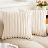 A close-up of a cream colored square faux rabbit fur cushion cover resting on a beige sofa.