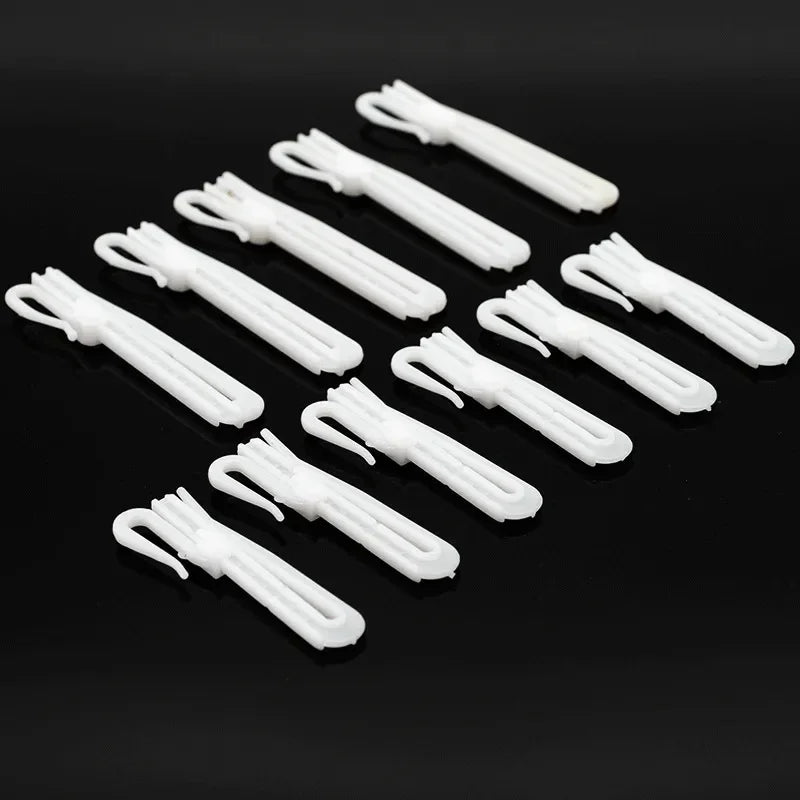 A collection of white adjustable curtain hanging hooks arranged diagonally on a dark surface.