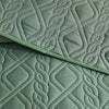 A close-up of a sage green quilted fabric, showing a diagonal fold and intricate wavy patterns.