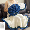 A woman models a white crochet blanket with blue and green floral trim, displayed as a bouquet.