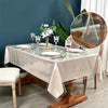 A glass table is set for a meal with white plates and silverware, protected by a clear PVC mat.