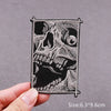 A black embroidered patch depicting a detailed skull design on a gray fabric background.