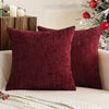 A deep burgundy chenille pillow cover resting on a white sofa next to a decorated Christmas tree.