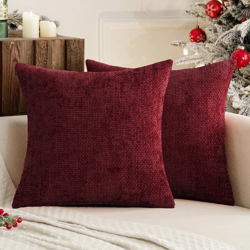 A deep burgundy chenille pillow cover resting on a white sofa next to a decorated Christmas tree.