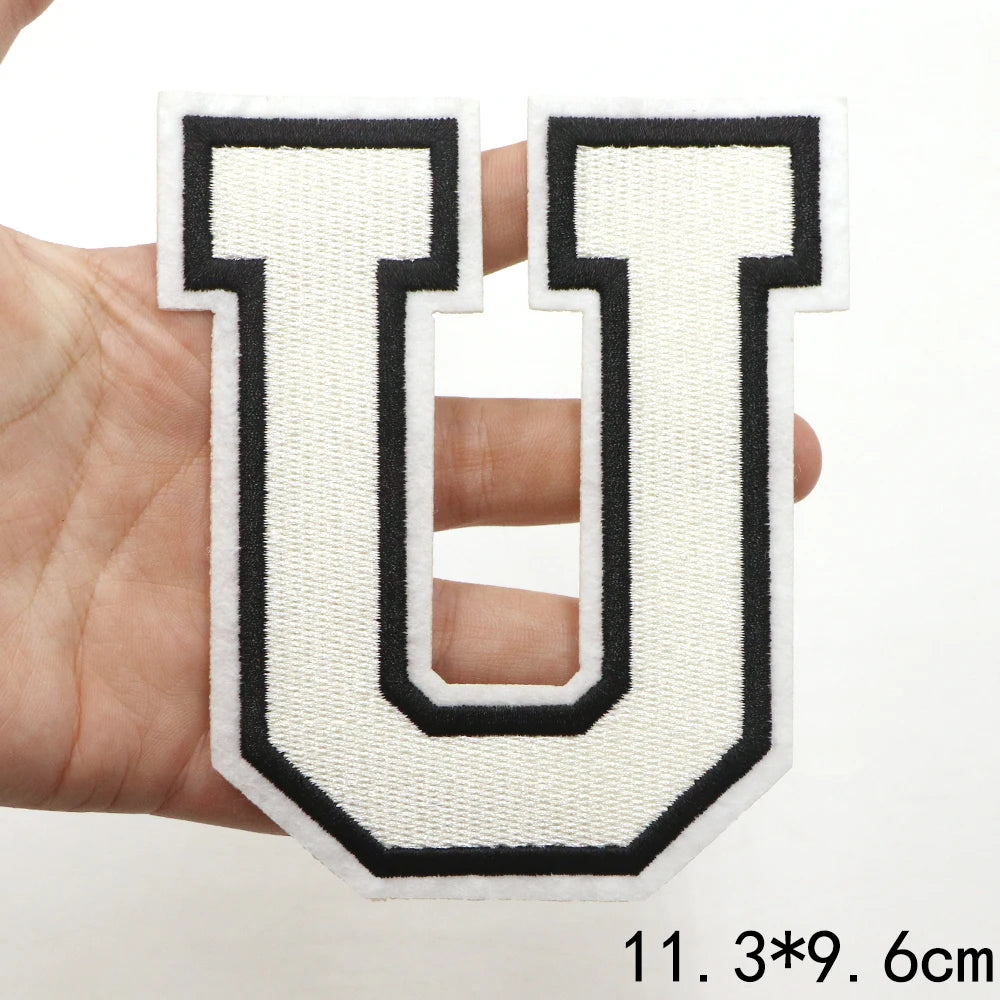 A hand holds a white letter patch shaped like the letter U with black outline and stitching.