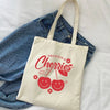 A cream canvas shopping bag featuring the text Delicious Cherries and two smiling cherry illustrations.