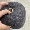 A hand is holding a ball of dark gray hand-woven wool and linen blended yarn.
