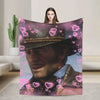 A person holds up a blanket featuring a portrait of a man in a hat surrounded by pink hearts.