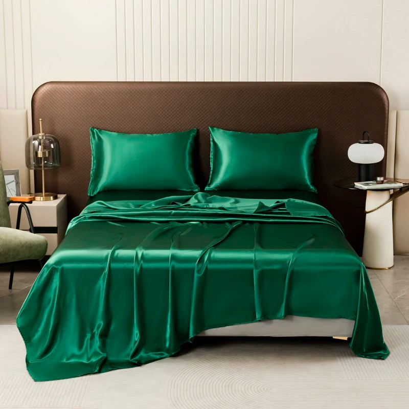 A luxurious emerald green satin flat bed sheet set with pillows and a draped sheet on a bed.