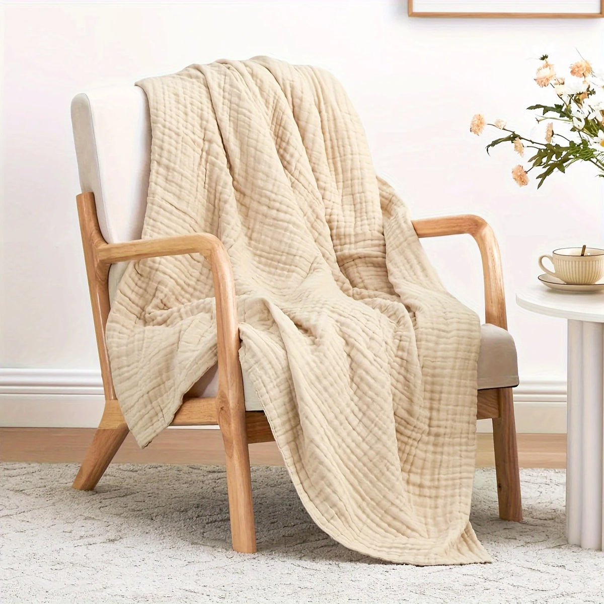 A beige woven blanket draped over a wooden armchair next to a white table.