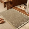 A beige waffle texture bath mat placed on a wooden floor next to a wooden cabinet.