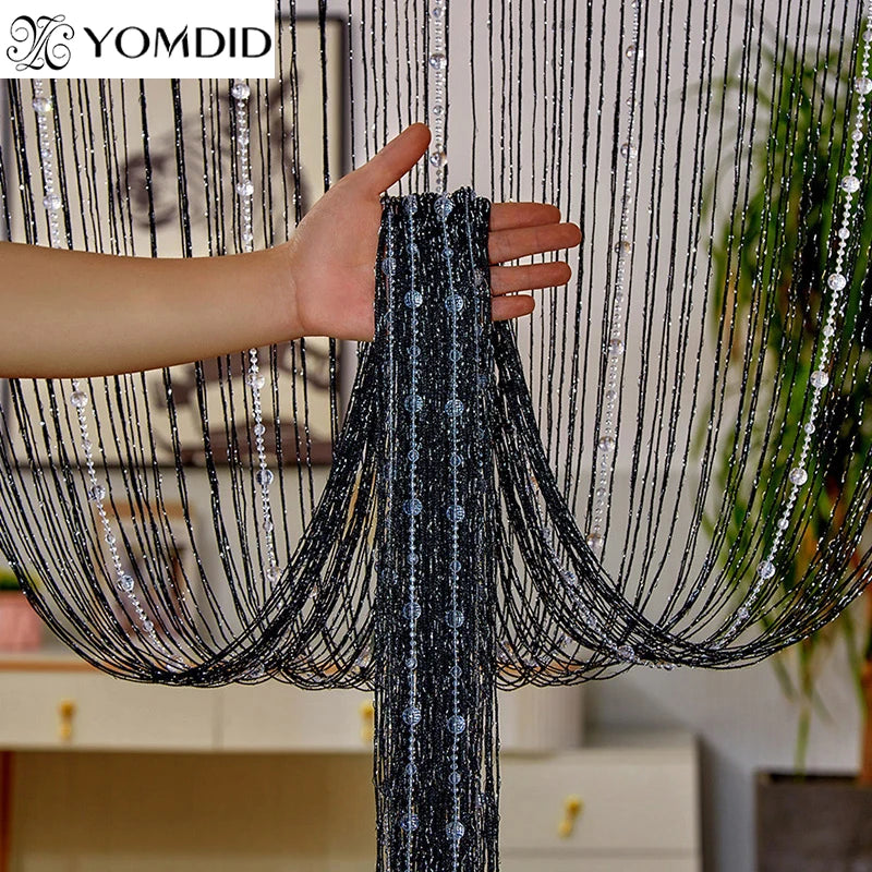 A hand is pulling a black crystal beaded string curtain with tassels down, showing the texture and drape of the fabric.
