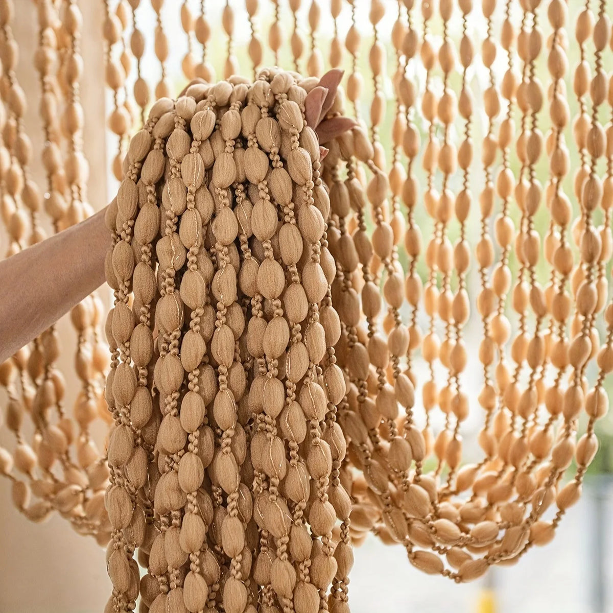 Close-up of a beige decorative fabric door curtain with a thick, braided tassel trim hanging.