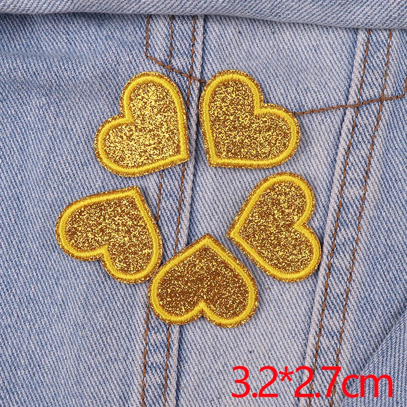 Five gold glitter heart patches sewn onto a light blue denim fabric.