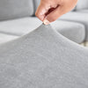 A hand is touching the fabric of a gray stretchable chenille sofa cushion cover.