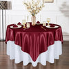 A maroon satin tablecloth is set for an elegant dining table with gold cutlery and white floral arrangements.
