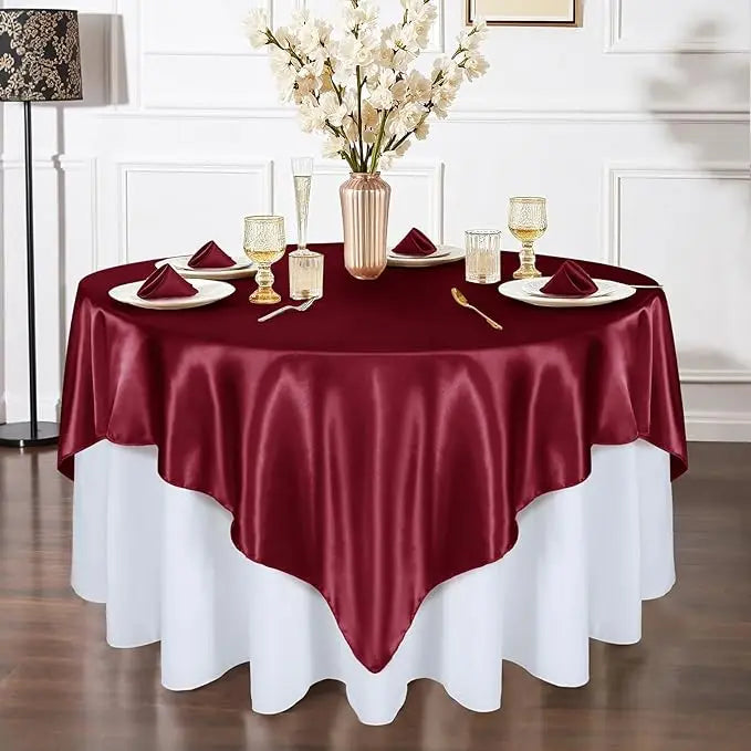 A maroon satin tablecloth is set for an elegant dining table with gold cutlery and white floral arrangements.