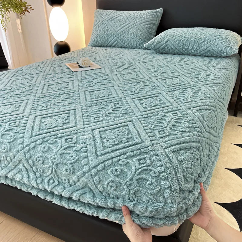 A teal plush jacquard mattress cover is displayed on a bed, folded and with pillows nearby.