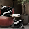 A decorative pillowcase with a black and white wavy geometric pattern resting on a pink armchair.