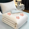 A white embroidered cooling summer quilt with pink floral designs is displayed on a light blue surface.
