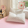 A pink bed features a white duvet cover and pillows with black polka dots, next to a decorative clock and a framed sign.