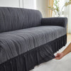A dark gray jacquard stretch sofa cover with vertical stripes is draped over a sofa.